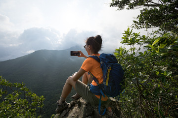 Successful hiker using smartphone on sunrise mountain top cliff edge