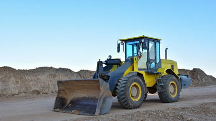 Front-end loader working at construction site. Earth-moving heavy equipment for road work. Public works, civil engineering, road building. Construction machinery for loading, lifting cargo