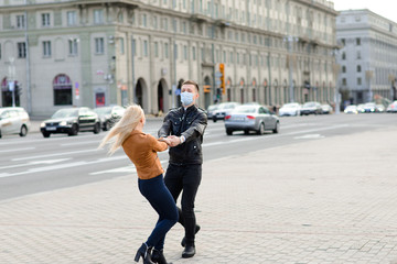 Obraz premium Couple in protective masks have a walk outdoors in the city near business building at quarantine time. Conception of coronavirus.