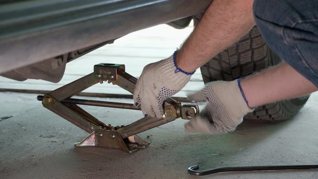 lifting the car with a jack screw to replace the wheel