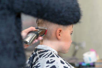 Happy boy is sitting in barber salon with wet hair and cuts her hair.