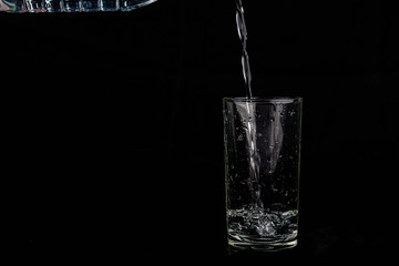 Close up pouring purified fresh drink water from the bottle isolated on black background