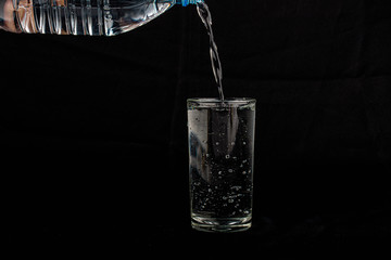Close up pouring purified fresh drink water from the bottle isolated on black background