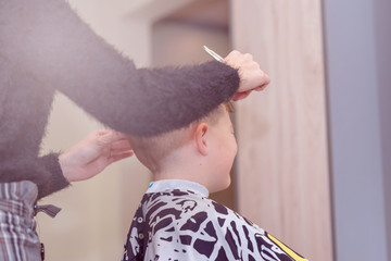 Cute boy getting haircut by hairdresser at the barbershop.Close up.