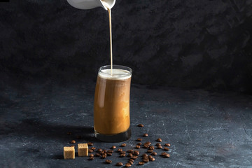Ice coffee frappe in tall glass. Cool summer drink on a dark background in low key. A stream of...