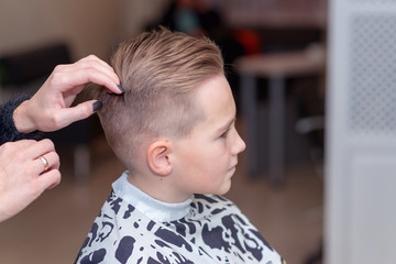 Nice european boy getting hairstyle in barbershop.hairdresser makes a hairstyle for a boy