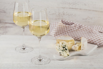 White wine served with cheese plate on light background. Two wineglasses of vino verde.