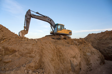 Excavator working at construction site on earthworks. Backhoe digs ground in pit for laying...