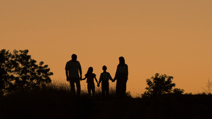 Fototapeta na wymiar Silhouette of a happy family of four, mother, father, daughter, son at sunset