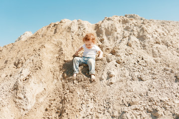 a small child with blond curly hair in a white T-shirt and blue jeans walks in the sunny desert during the day