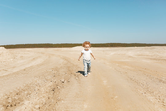 A little girl at the age of 2 walks along the sandy desert in jeans and a white T-shirt. Clear sunny day.