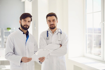 Two practicing doctors with clipboard standing in a clinic office.