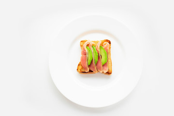 Avocado and salmon sandwich on toasted bread on a white plate. White background
