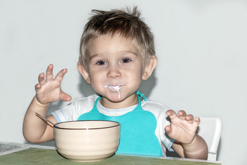 A child 1-2 years old eats. Portrait of a happy toddler boy with spoon at the kitchen table. Toned. close-up.