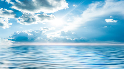 Fototapeta na wymiar Sea landscape, sea surface. Blue sky, clouds, sunlight, rays. Empty natural scene in the open air. Blurred abstract background. Background of a sea landscape. Blue sky with clouds over the sea. 