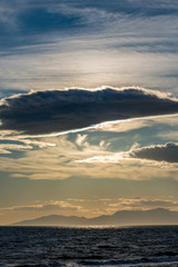 Sun is hidden behind curly clouds near the fishermen village of Porto Lagos, Northern Greece. Mountain range in haze and sea water in darkness. Dynamic landscape seascape with high contrast