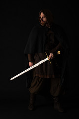 medieval Scottish man in mantel with sword in dark isolated on black
