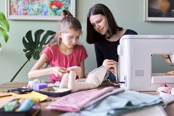Family, two girls sisters teenager and younger together sewing toy doll bunny