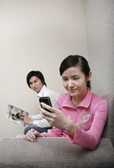 Woman using mobile phone while man is reading magazine