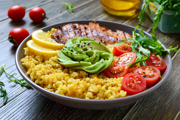 Bulgur with grilled chicken breast, fresh vegetables, avocado, arugula. Diet lunch on a wooden table. Healthy food.