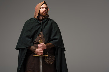 medieval Scottish redhead knight in mantel with sword on grey background