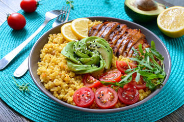 Bulgur with grilled chicken breast, fresh vegetables, avocado, arugula. Diet lunch on a wooden table. Healthy food