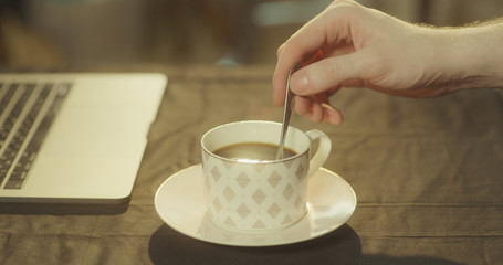 Man stirs his black coffee in the morning using a silver spoon