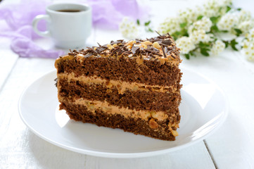 Chocolate cake with nut cream on a white wooden table. A piece of cake on a plate and a cup of coffee.