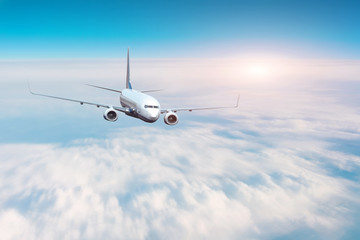 Passenger plane flies high above the clouds in the blue sky.