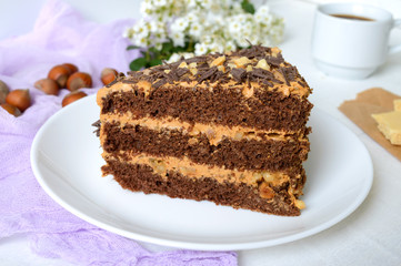 Chocolate cake with nut cream on a white wooden table. A piece of cake on a plate and a cup of coffee.