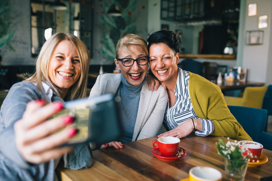 women friends having coffee break at cafe, taking pictures with smartphone