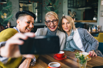 women friends having coffee break at cafe, taking pictures with smartphone