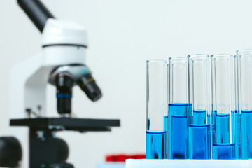 Microscope and test tubes on table in laboratory, close up