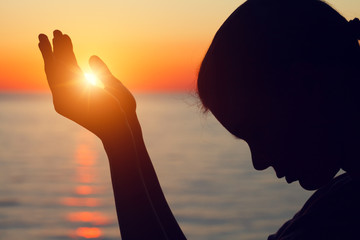silhouette of young woman raising hands praying at sunset or sunrise light, yoga practice,...