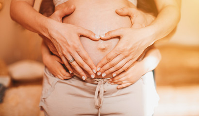 Couple at home holding a pregnant woman's belly. Cropped image of beautiful pregnant woman and her handsome husband hugging the tummy.