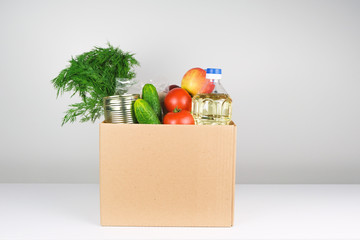 Donation box with food, open card box with oil, apples, cucumbers, tomatoes and canned food.