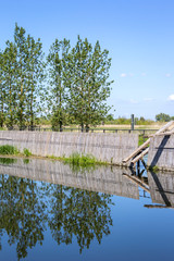 View of an historical weir system. In the background there is a row of poplars.
