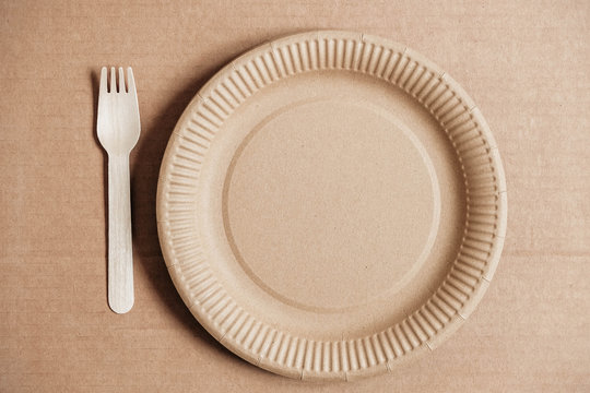 Wooden fork and plate on kraft paper background. Eco friendly disposable tableware. Also used in fast food, restaurants, takeaways, picnics. Top view. Copy, empty space for text