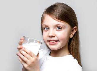 A happy girl with a glass of milk, smiling cheerfully with a beautiful smile. World milk day. Portrait of a child with a Cup of milk. Products for human health. Healthy food. Space for text