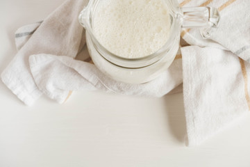 Glass jug with milk and napkin on a white table. Top view. Copy, empty space for text