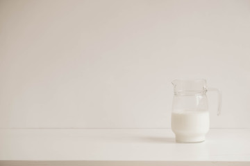 Glass jug with milk on a white table. Copy, empty space for text