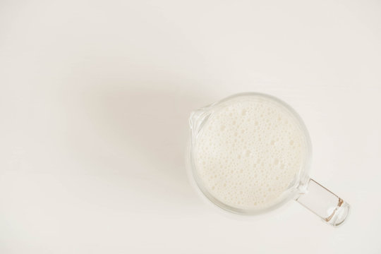 Glass jug with milk on a white table. Top view. Copy, empty space for text
