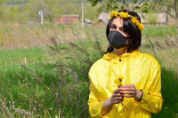 Brunette woman in yellow jacket with wreath of dandelions and medical black mask holding bouquet of 
dandelions. looking at camera. coronavirus pandemic concept.