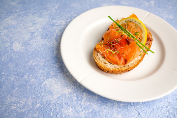 Norwegian smoked salmon with lemon slice, chives and sprouts decoration on a white plate with blue textured backdrop. Food photography with sidelight.