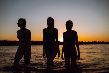 Silhouette of three young girls come out of the sea at sunset. Summer holidays, vacation, relax and lifestyle concept.