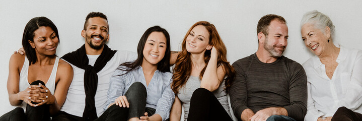 Group of cheerful diverse people sitting on a floor in a white room