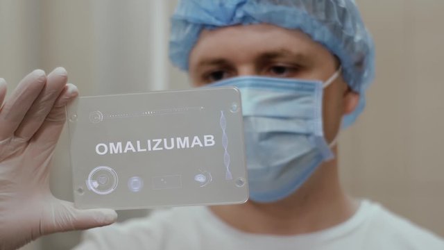 Doctor in face mask interacts futuristic hud screen tablet with text Omalizumab. Medical concept of future technology. Futuristic doctor with modern medical care gadget