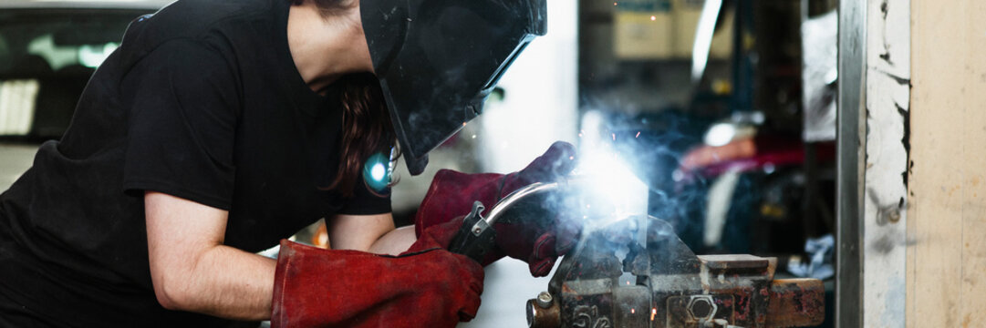 Female welding a metal piece in the garage - Powered by Adobe