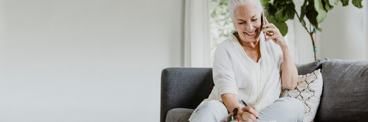 Cheerful elderly woman talking on a phone on a couch