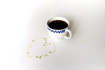 On a white background is a coffee mug and a heart of white flower petals is laid out next to it.